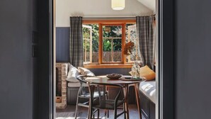 Une pièce comprenant une table à manger, des chaises, un banc, un luminaire suspendu et une fenêtre avec des rideaux.