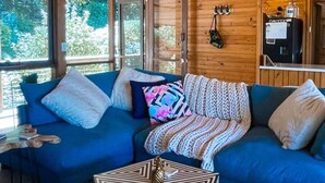 A cozy cabin interior with a blue sofa, a geometric coffee table, and a wooden ceiling.
