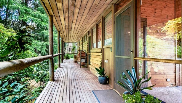 A wooden deck with a railing, potted plants, and a shoe rack.