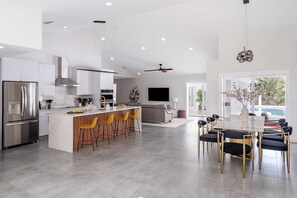 A modern kitchen with a central island, a dining area with a marble table, and a large window overlooking a pool. - 2 Villas, Pickleball,Heated pool, Naples escape. (Naples)