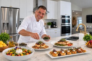 A modern kitchen with stainless steel appliances, a marble countertop, and a chef preparing food. - The Estates by Naples Escape | 2 Private Villas,Heated Pool, Spa, Pickleball (Naples)