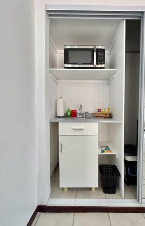 Una kitchenette compacta con microondas, un refrigerador pequeño, un lavamanos y un armario de almacenamiento.