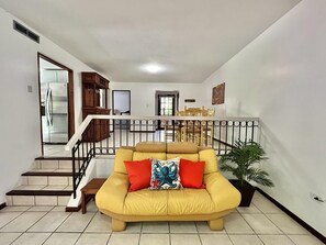 A living room with a yellow sofa, a staircase, and a dining area in the background. - Beach Life Casita A - Parking&Wifi (Palmas del Mar)