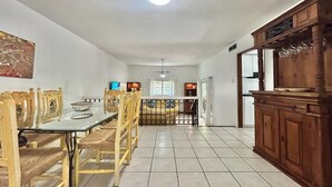 Uma área de refeições com uma mesa de vidro, cadeiras de vime, um armário de madeira e um ventilador de teto.