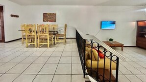 Uma sala de estar espaçosa com área de jantar, sofá, TV fixada na parede e escada que leva a outro andar.
