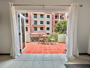 A balcony with a tiled floor, a table, and chairs, overlooking a building with balconies and a palm tree.