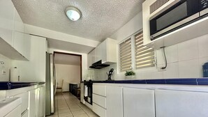 Uma cozinha moderna com armários brancos, micro-ondas e piso revestido de azulejos.