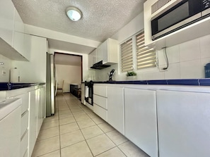 A modern kitchen with white cabinetry, a microwave, and a tiled floor.