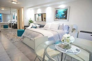 A modern bedroom with a bed, bedside table, and a glass table with flowers. - Beautiful Beach Studio @Condado (San Juan)