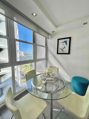 Un espace repas moderne avec une table et des chaises en verre, un vase de fleurs et une œuvre d’art encadrée accrochée au mur.