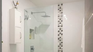 Et moderne badeværelse med brusekabine i glas, et hvidt toilet og en vask med spejl.