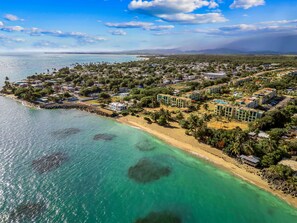 An aerial view of a coastal resort with beachfront villas, a marina, and lush greenery.