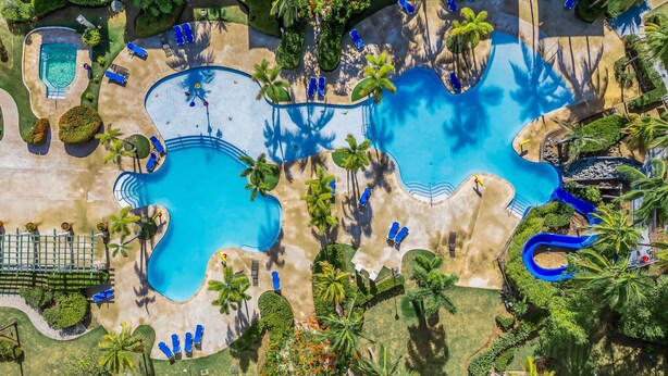 Luchtbeeld van een resort met meerdere zwembaden, palmbomen en loungegedeeltes.