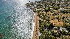 Luchtbeeld van een kustresort met strandvilla's, een zandstrand en een helder uitzicht op de oceaan.