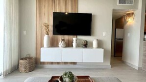 Una sala de estar moderna con un televisor de pantalla plana montado en una pared de paneles de madera, un sofá gris y una bandeja de madera con una planta.