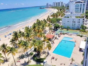 A beach resort with a swimming pool, palm trees, and a view of the ocean.