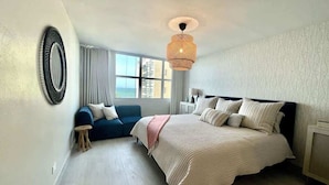 Un dormitorio con una cama grande, un sofá azul, una mesita auxiliar pequeña y un ventanal con vistas.