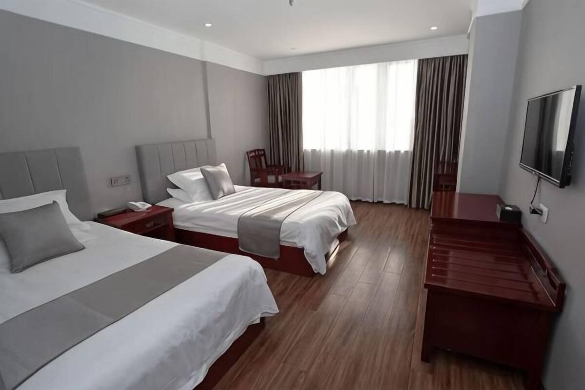 Habitació d'hotel amb un llit gran, una taula, una cadira, un televisor i una finestra amb cortines.