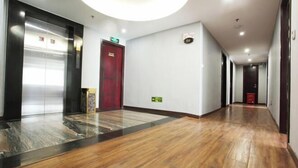 En hotellobby med trægulv, elevator og en rødlakeret dør.
