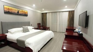 A hotel room with a bed, a desk, a chair, a TV, and a painting on the wall. - Junyue Hotel (Yueqing)