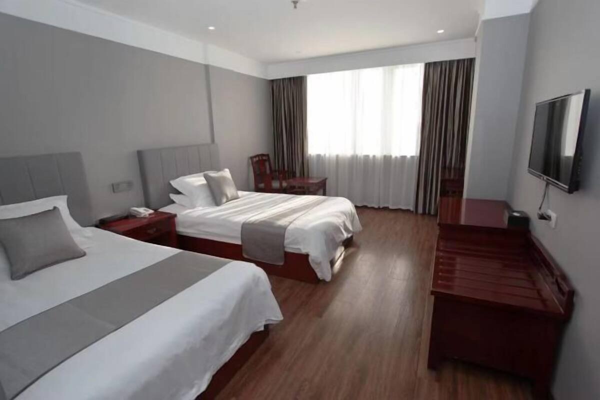 Habitació d'hotel amb dos llits, televisió, escriptori i finestra amb cortines.