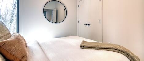 A bedroom with a bed, a round mirror, a wardrobe, and a window.