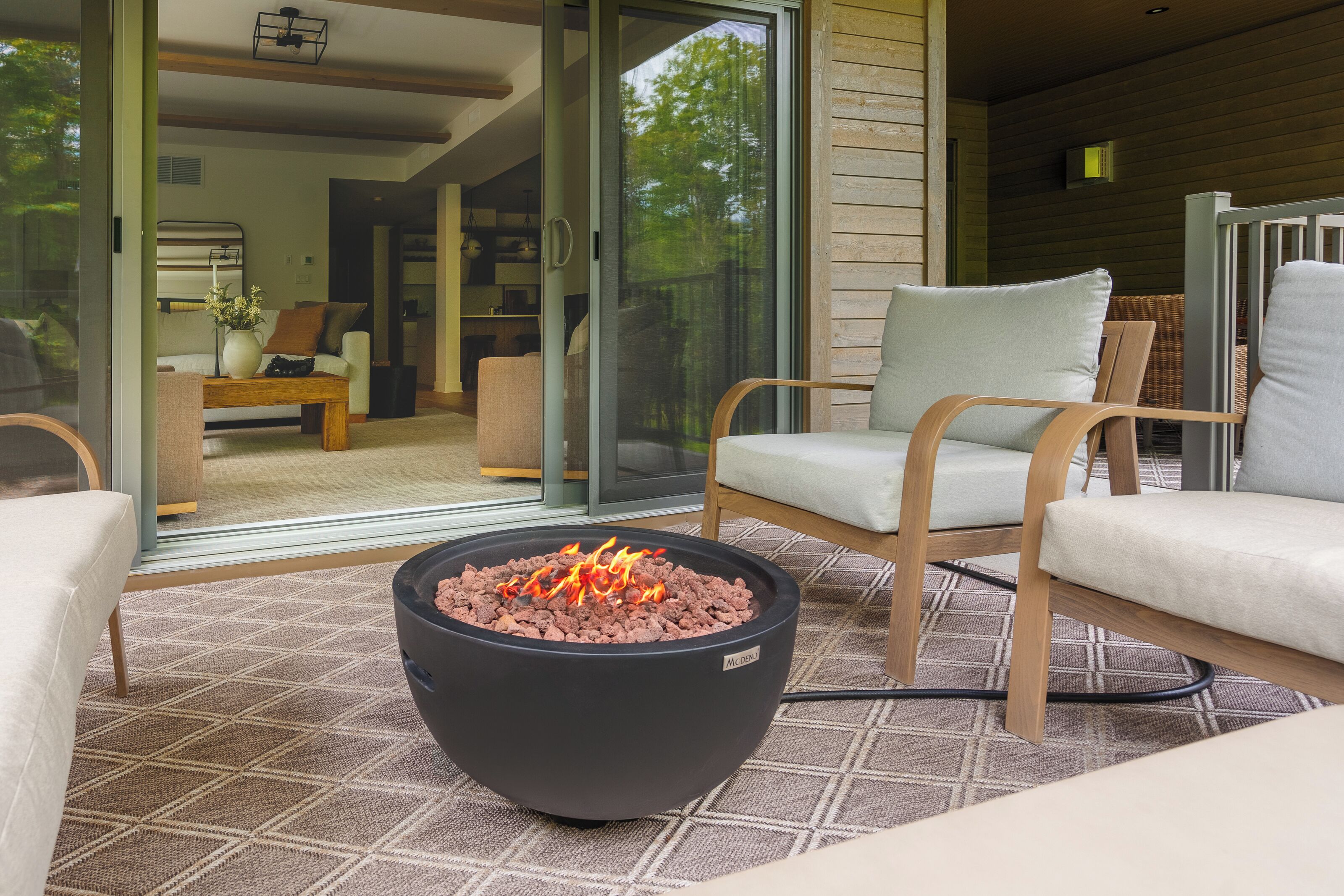 A cozy outdoor seating area with a fire pit, comfortable chairs, and a glass door leading to an interior space.