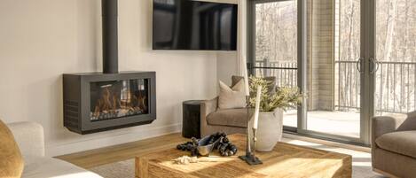 A modern living room with a fireplace, a flat-screen TV, and a large sliding glass door to the outdoors.