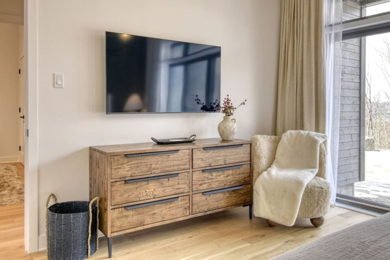 Un soggiorno moderno con un mobiletto in legno, una televisione a parete e una poltrona confortevole.