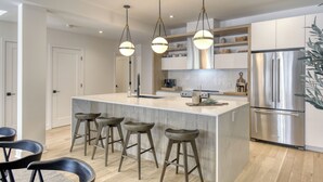 A modern kitchen with a central island, bar stools, stainless steel appliances, and pendant lighting. - 105 Verbier Building 14 (Mont-Tremblant)
