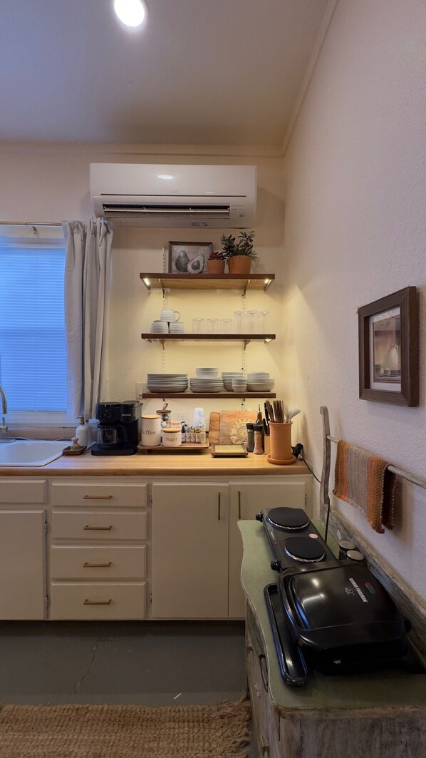 A kitchen with a stove, sink, and shelves with kitchenware.