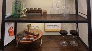 Una estantería de madera con una lámpara de estilo rústico hecha con una rama, una botella, vasos y una bandeja de madera con un abridor.