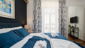Una habitación de hotel con una cama, un televisor, un estante con objetos y un cuadro en la pared.