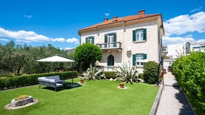 A two-story house with a well-maintained lawn, outdoor seating, and a pathway leading to the entrance.