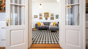 A living room with a checkered floor, a grey sofa with yellow cushions, and a wall adorned with framed pictures.