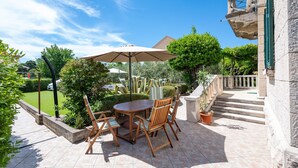 An outdoor patio with a round wooden table and chairs, a large umbrella, and a potted plant.