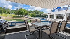 Un espace extérieur aménagé, abrité et doté d’une table et de chaises, offrant une vue sur une étendue d’eau et un bateau amarré.