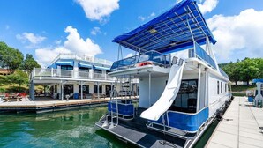 Une péniche flottante dotée d’une terrasse couverte, d’un toboggan et d’une zone d’amarrage avec des sièges extérieurs.