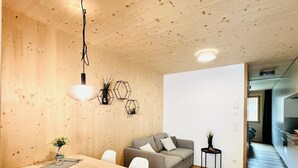 A modern interior with a wooden ceiling, a dining table with chairs, a grey sofa, and a small side table with a plant. - Appartement Johann - Mellau - Urlaub im Herzen des Bregenzerwaldes (Mellau)