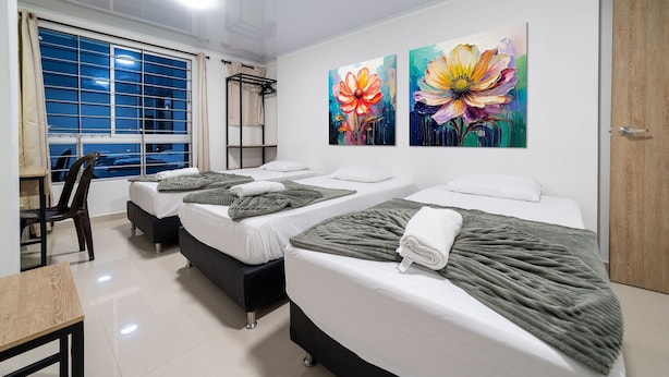 A hotel room with three beds, a desk, and a chair. There are two large floral paintings on the wall. - DOXA HOTEL (Medellín)
