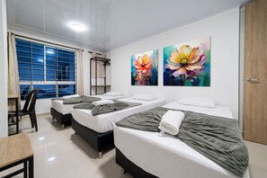 Habitación de hotel con tres camas, un escritorio y una silla. Dos grandes cuadros florales adornan la pared.