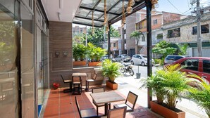 An outdoor patio with tables and chairs, potted plants, and a view of the street. - DOXA HOTEL (Medellín)
