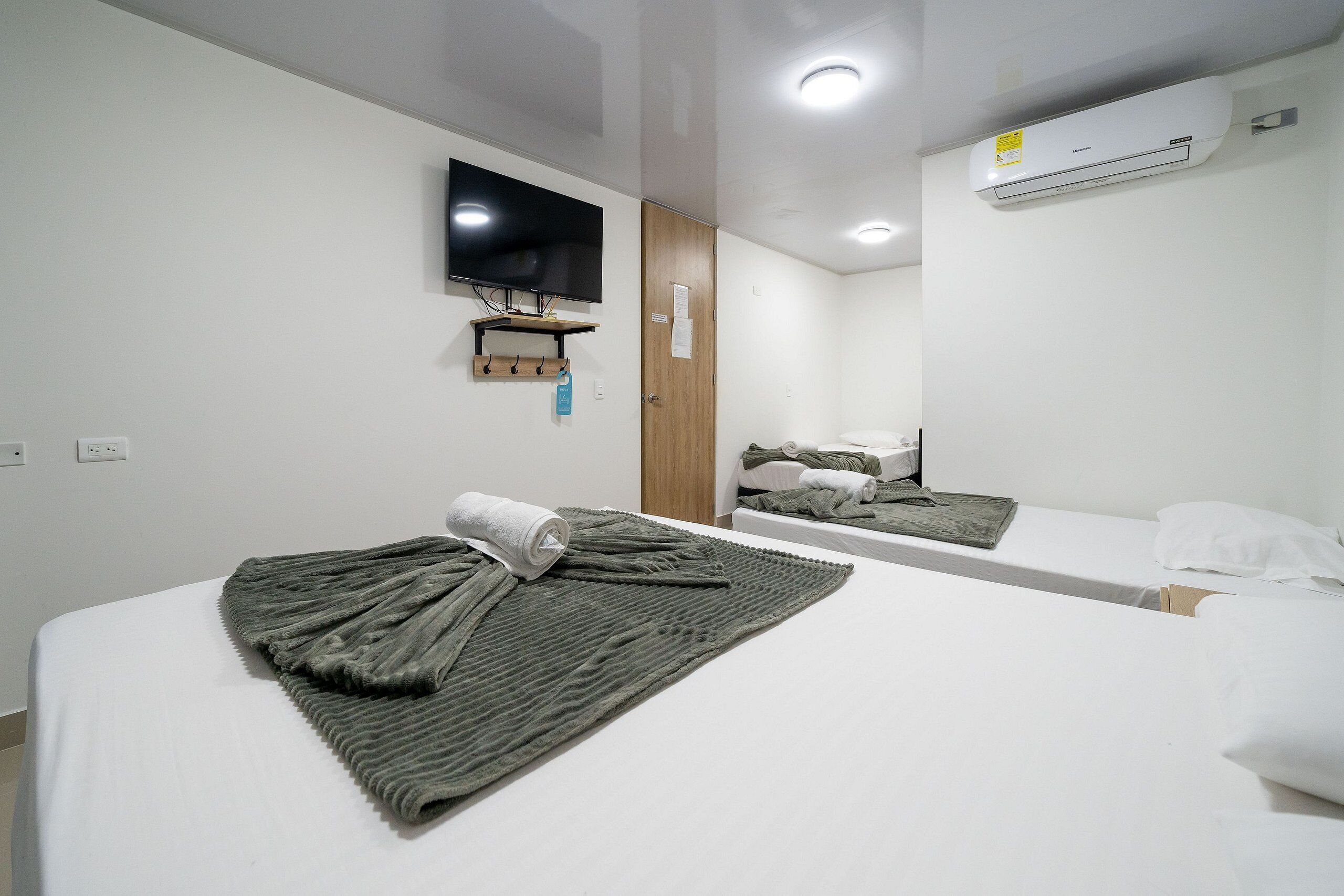A hotel room with a bed, a TV mounted on the wall, and an air conditioning unit.