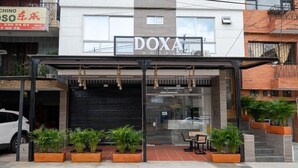 A hotel with a modern facade, a covered entrance, and outdoor seating area with potted plants. - DOXA HOTEL (Medellín)