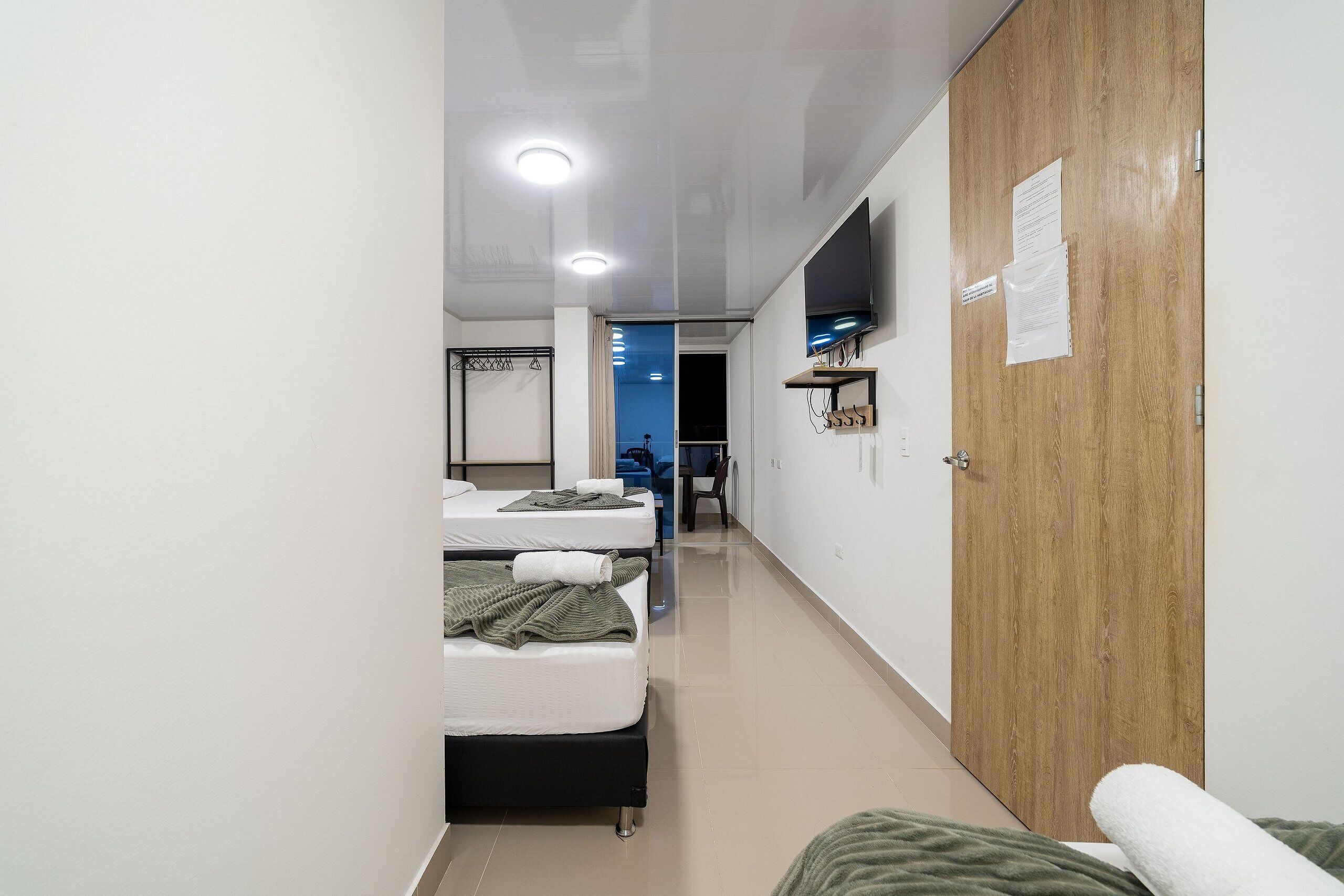 Habitación de hotel con armario de madera, televisor de pantalla plana montado en la pared y cama con manta verde.