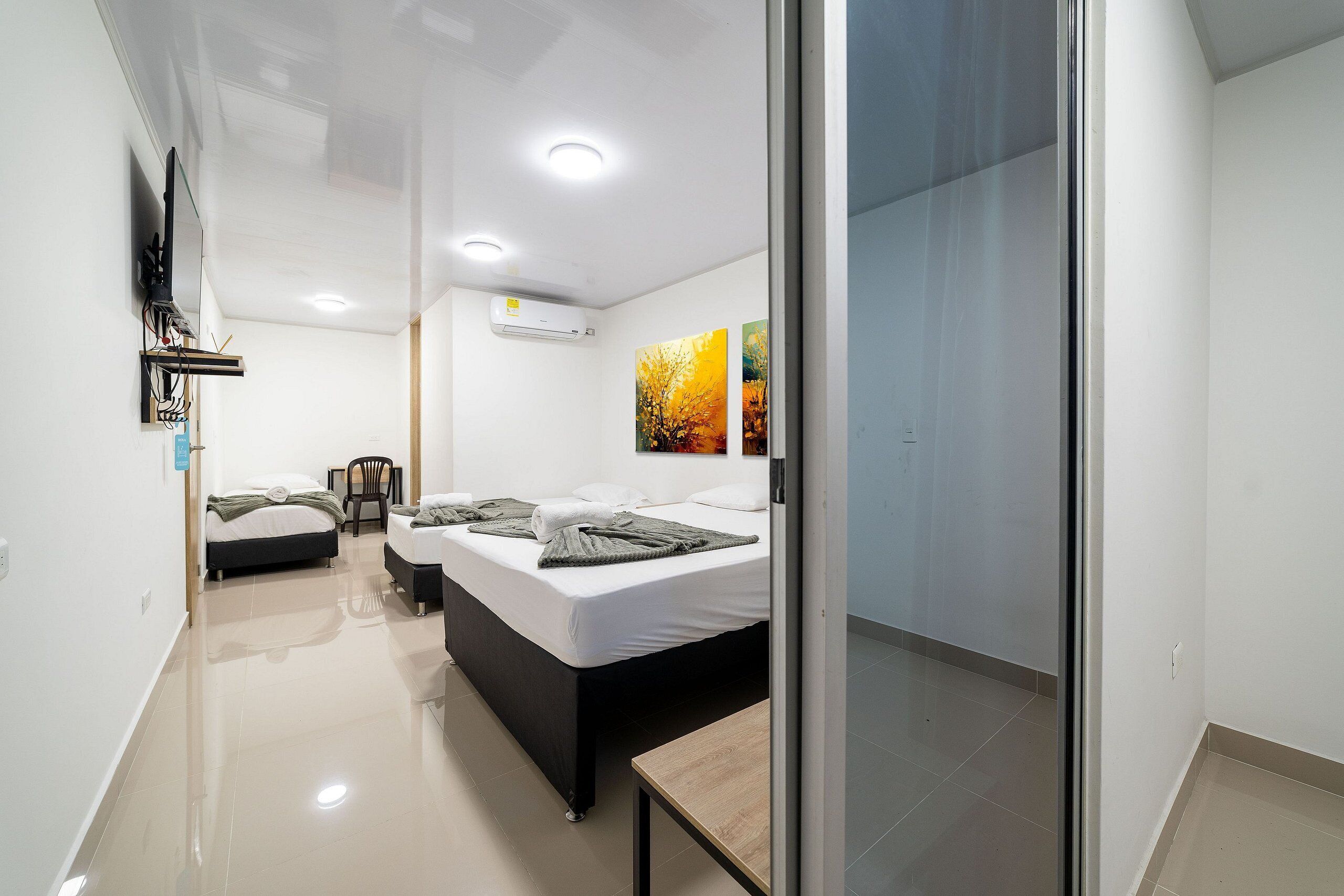 A modern bedroom with two beds, a flat-screen TV mounted on the wall, and a ceiling-mounted air conditioner.