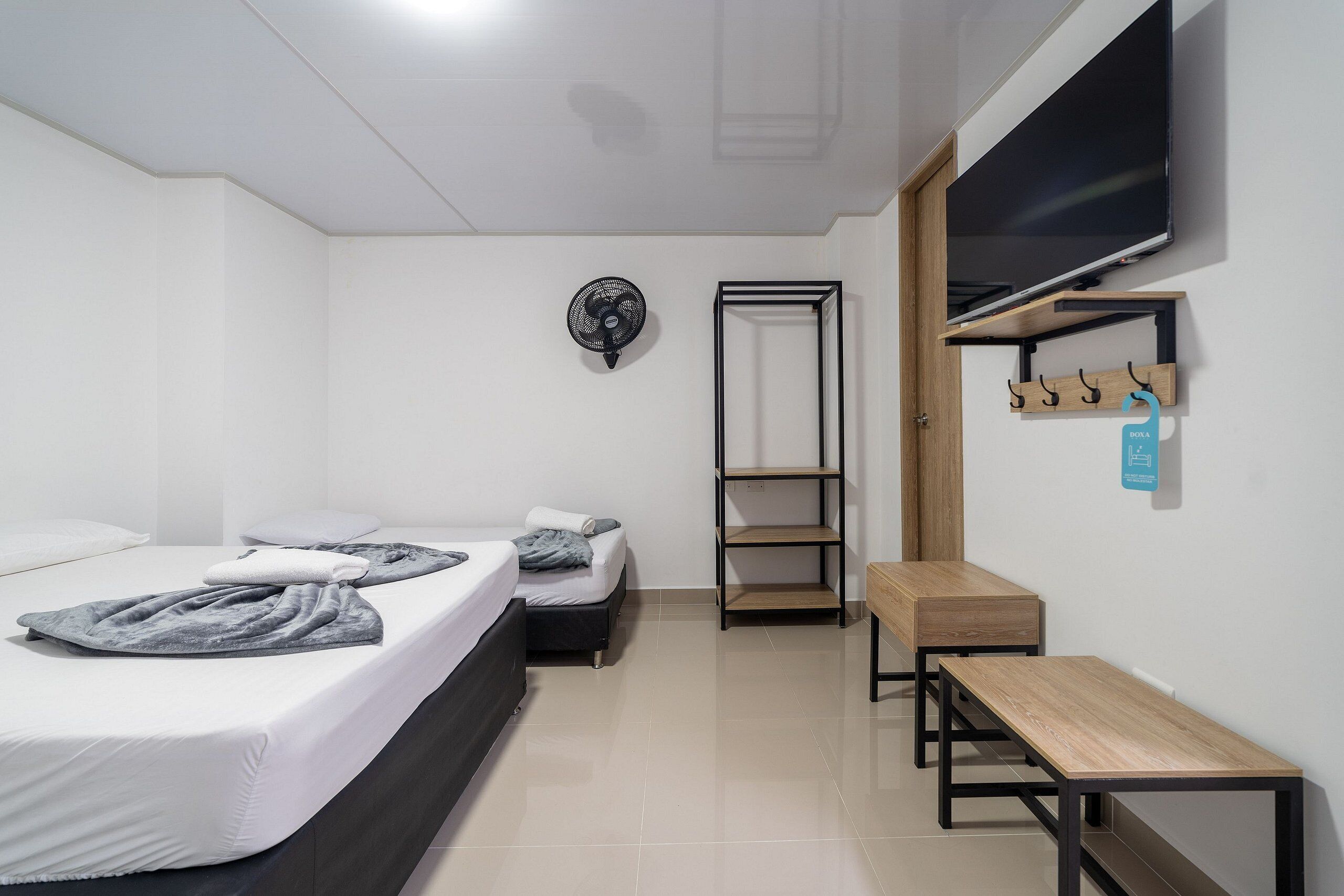 Una habitación de hotel moderna con cama, escritorio, televisor y repisa con ganchos.