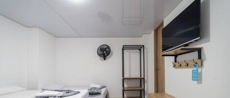 Una habitación de hotel moderna con cama, escritorio, televisor y repisa con ganchos.
