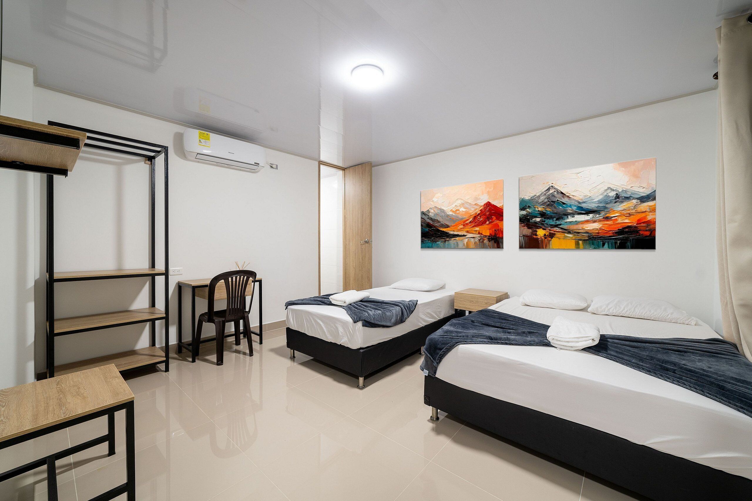 A modern hotel room with two beds, a desk, a chair, and artwork on the walls.