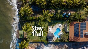 An aerial view of a coastal property with a swimming pool, solar panels, and a beach area. - Beira Mar-Cozinheira-Piscina-4QT-SH029 (Sirinhaem)